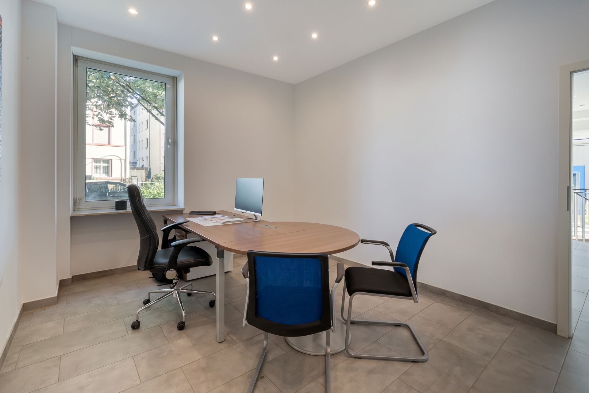 Helles Arbeitszimmer mit rundem Tisch, drei Stühlen und Computer am Fenster.