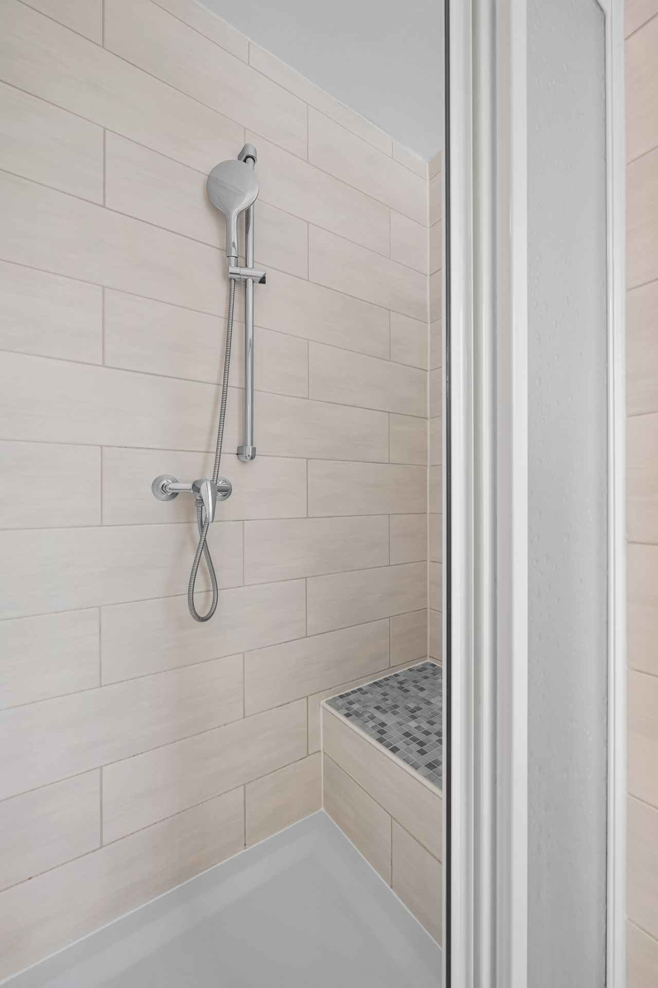 Moderne Dusche mit heller Fliesenwand, Handbrause und gefliestem Sitz.