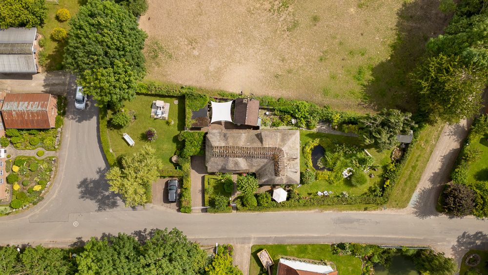 Luftaufnahme eines Wohnhauses mit Garten, Teich und umliegender Straße.