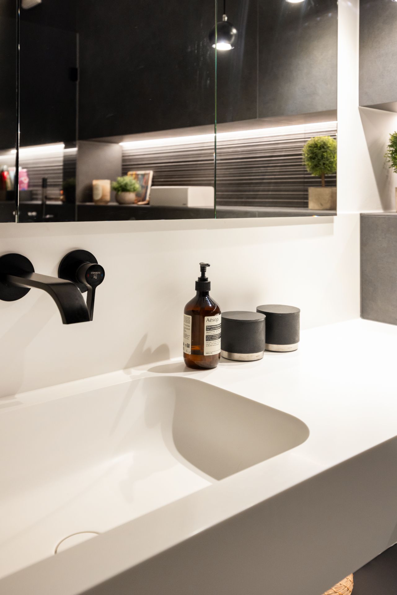 Modernes Badezimmer mit weißem Waschbecken, schwarzen Armaturen und Seifenspender.