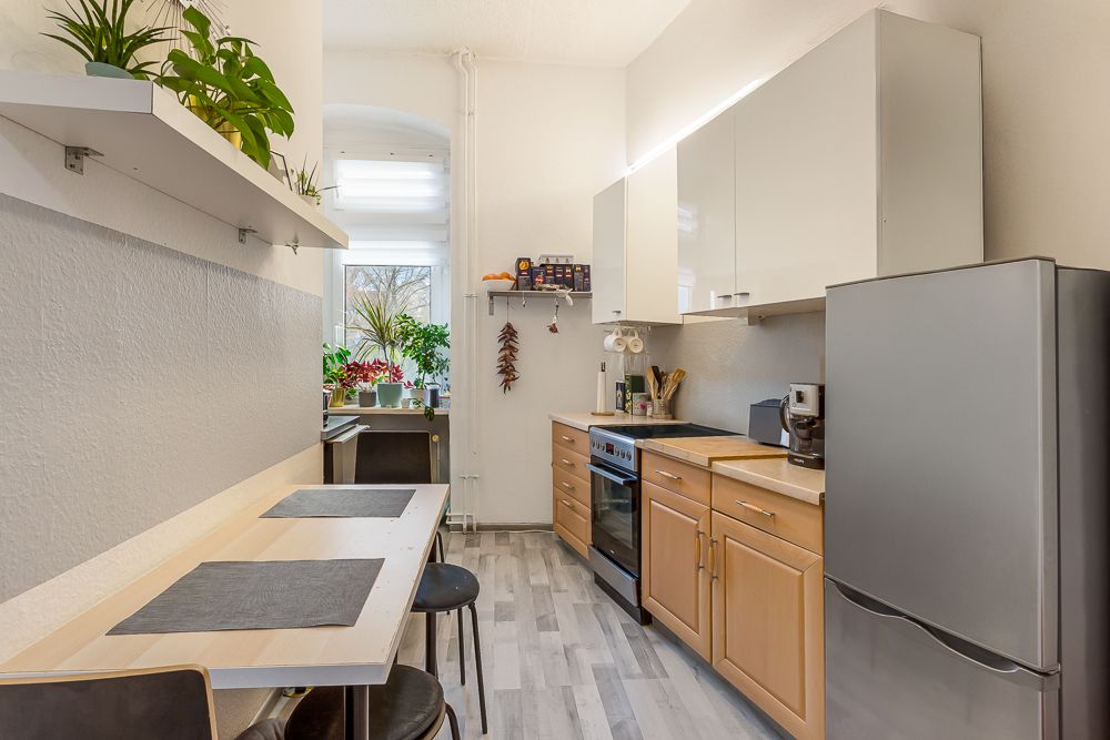 Moderne Küche mit Holzmöbeln, Esstisch, Kühlschrank und Pflanzen am Fenster.