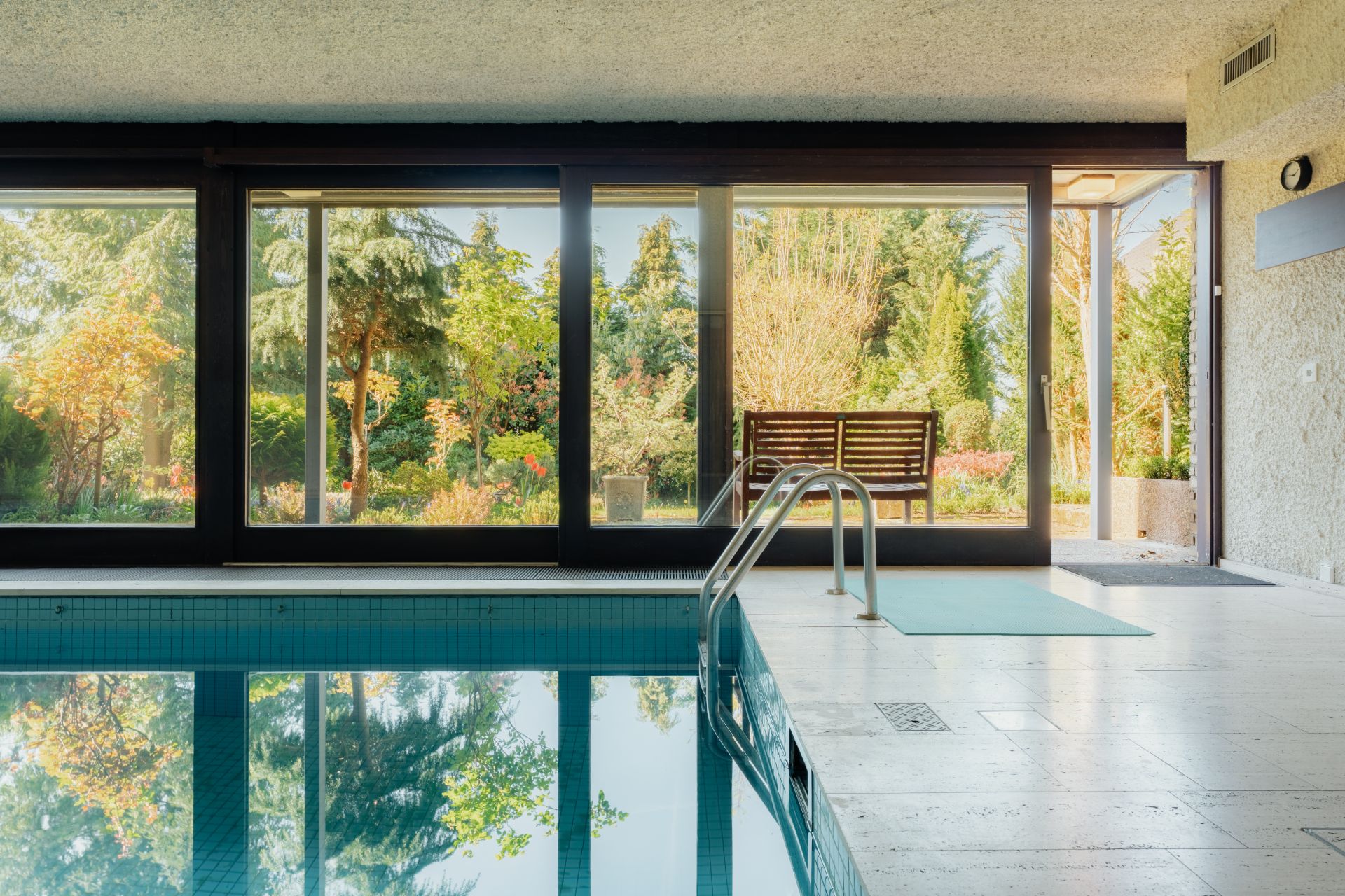 Innenpool mit großer Fensterfront und Blick auf einen grünen Garten.