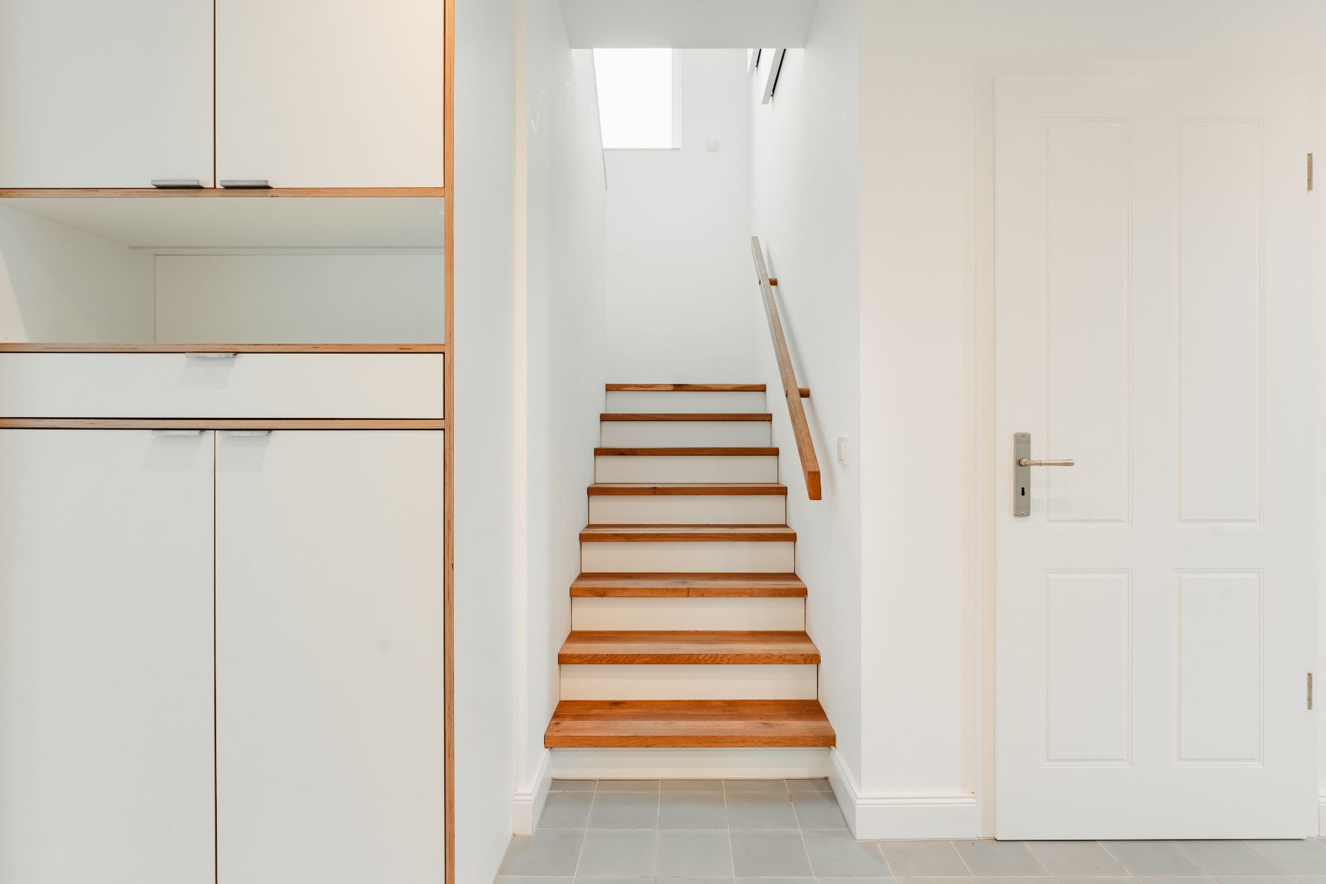 Heller Flur mit Holztreppe, weißer Tür und Einbauschrank.