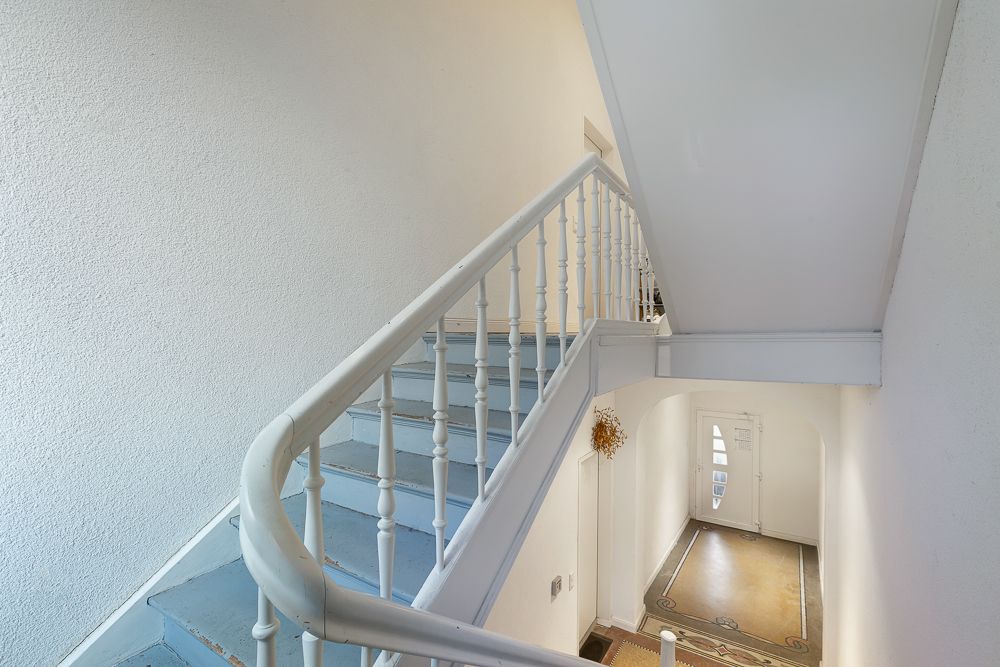 Helles Treppenhaus mit blau-grauer Treppe und Eingangstür mit Glaseinsatz.