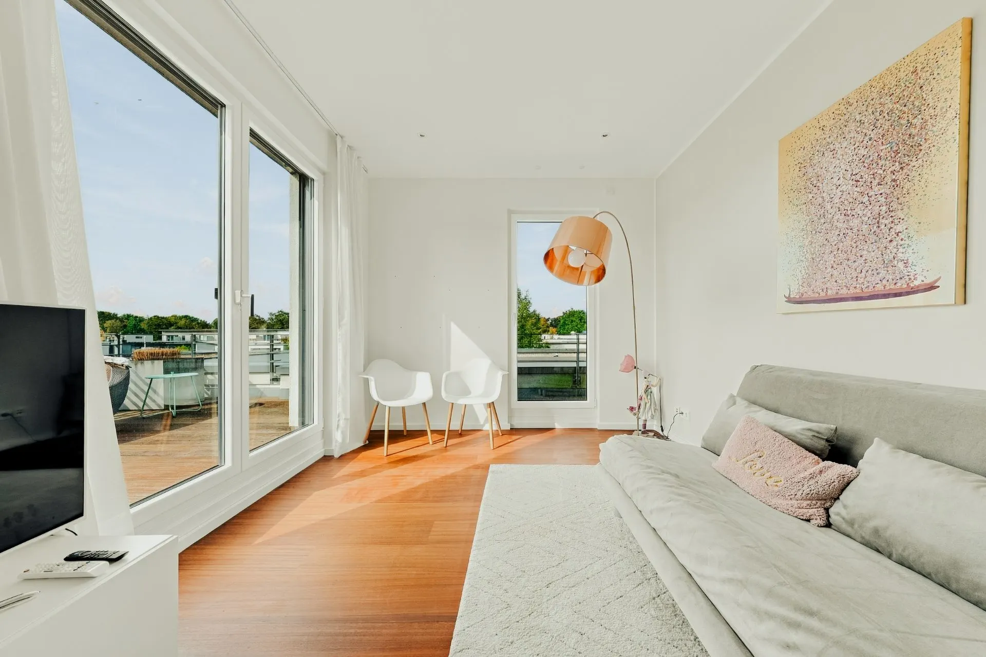 Helles Wohnzimmer mit großem Fenster, Sofa, zwei Stühlen, Stehlampe und Teppich.