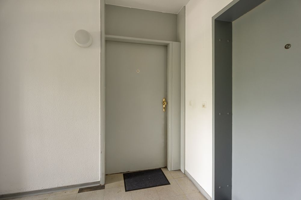 Hausflur mit grauer Wohnungstür, Fußmatte und hellem Fliesenboden.