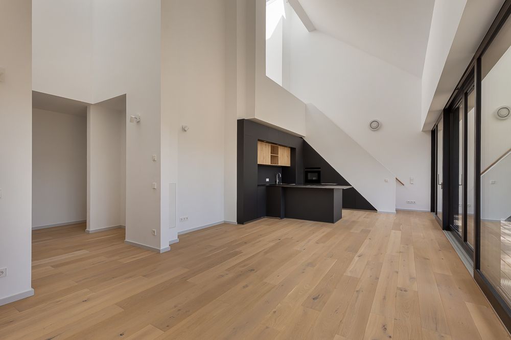 Heller Wohnraum mit Holzfußboden, offener Küche und großen Fenstern.