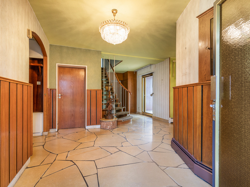 Heller Flur mit Kronleuchter, Holzvertäfelung und Wendeltreppe.