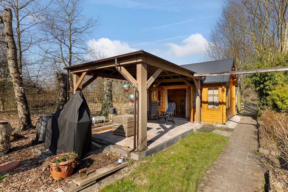 Holzhaus mit überdachter Terrasse, Gartenmöbeln und umliegendem Garten bei sonnigem Wetter.