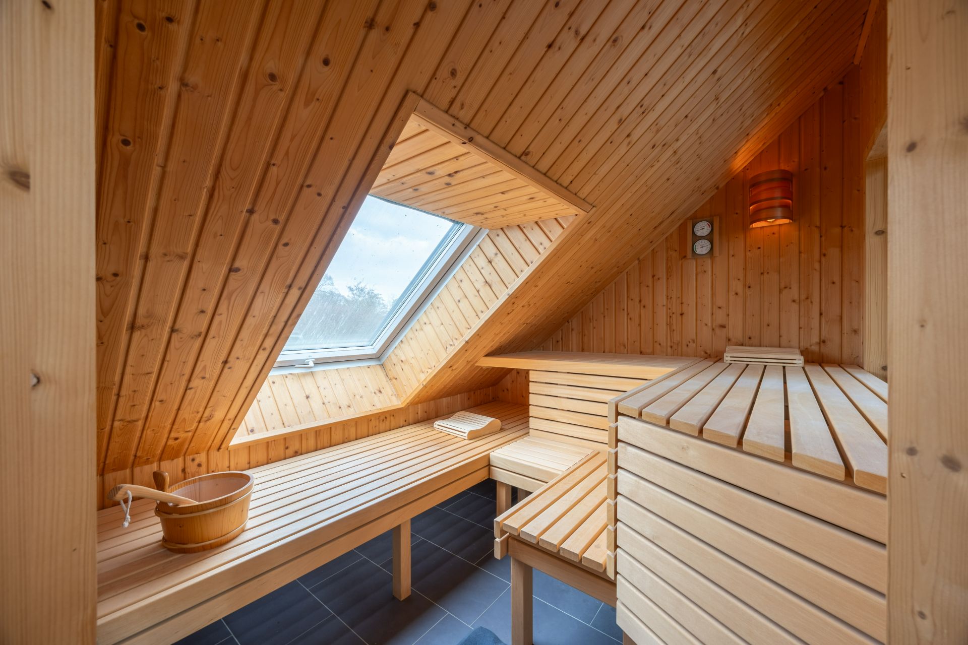 Holzsauna mit großem Fenster im Dachgeschoss und Sitzbänken.