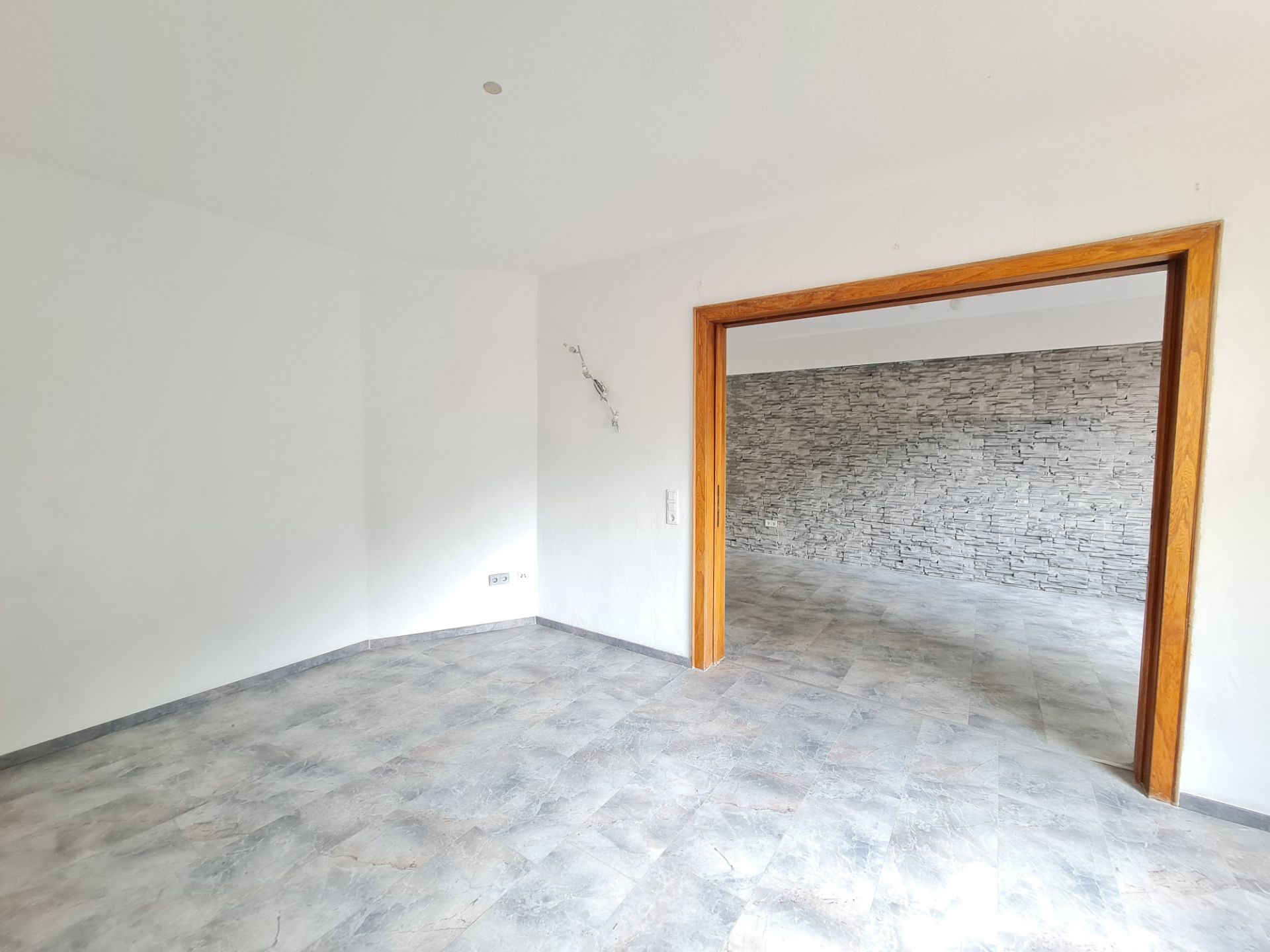 Leerer Raum mit Fliesenboden, weißer Wand und offener Tür zu Raum mit Steinwand.