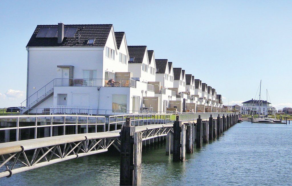 Moderne weiße Reihenhäuser am Wasser mit Steg und Booten im Hintergrund.