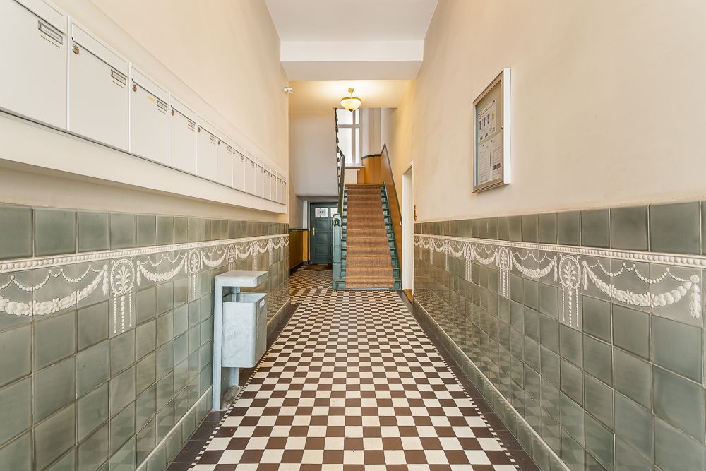 Eingangsbereich mit kariertem Fliesenboden, grünen Wandfliesen und Treppe am Ende.