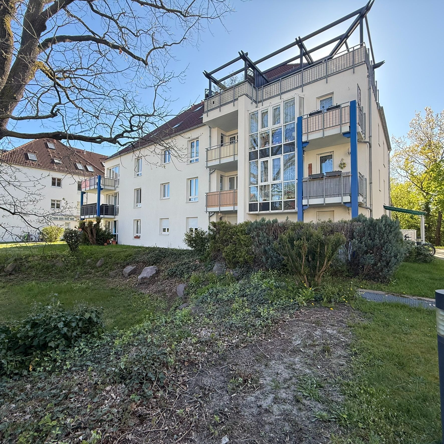 Mehrfamilienhaus mit mehreren Balkonen und verglastem Treppenhaus, umgeben von Grünfläche.