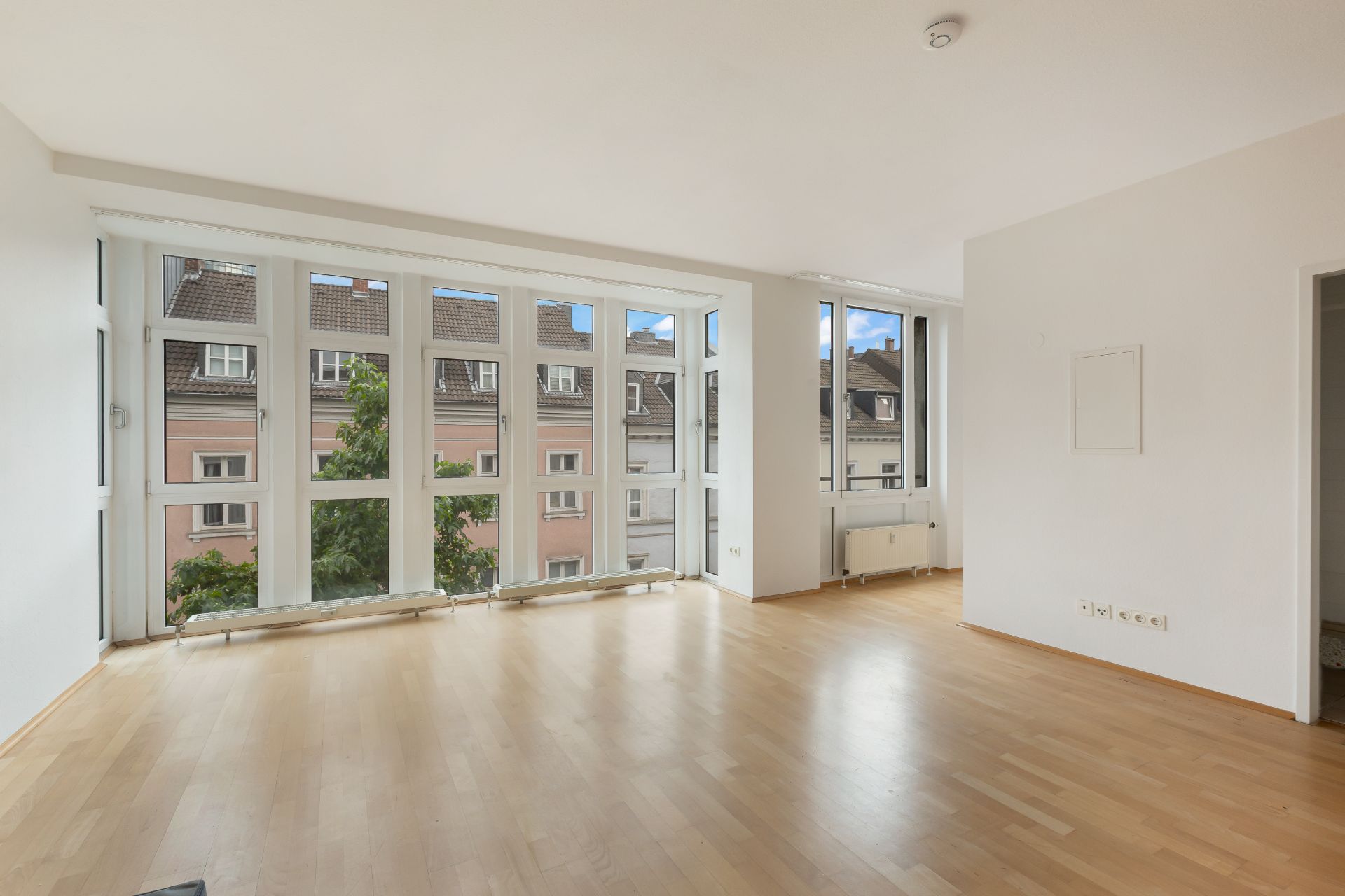 Helles Wohnzimmer mit großen Fenstern und Parkettboden, Blick auf Nachbargebäude.