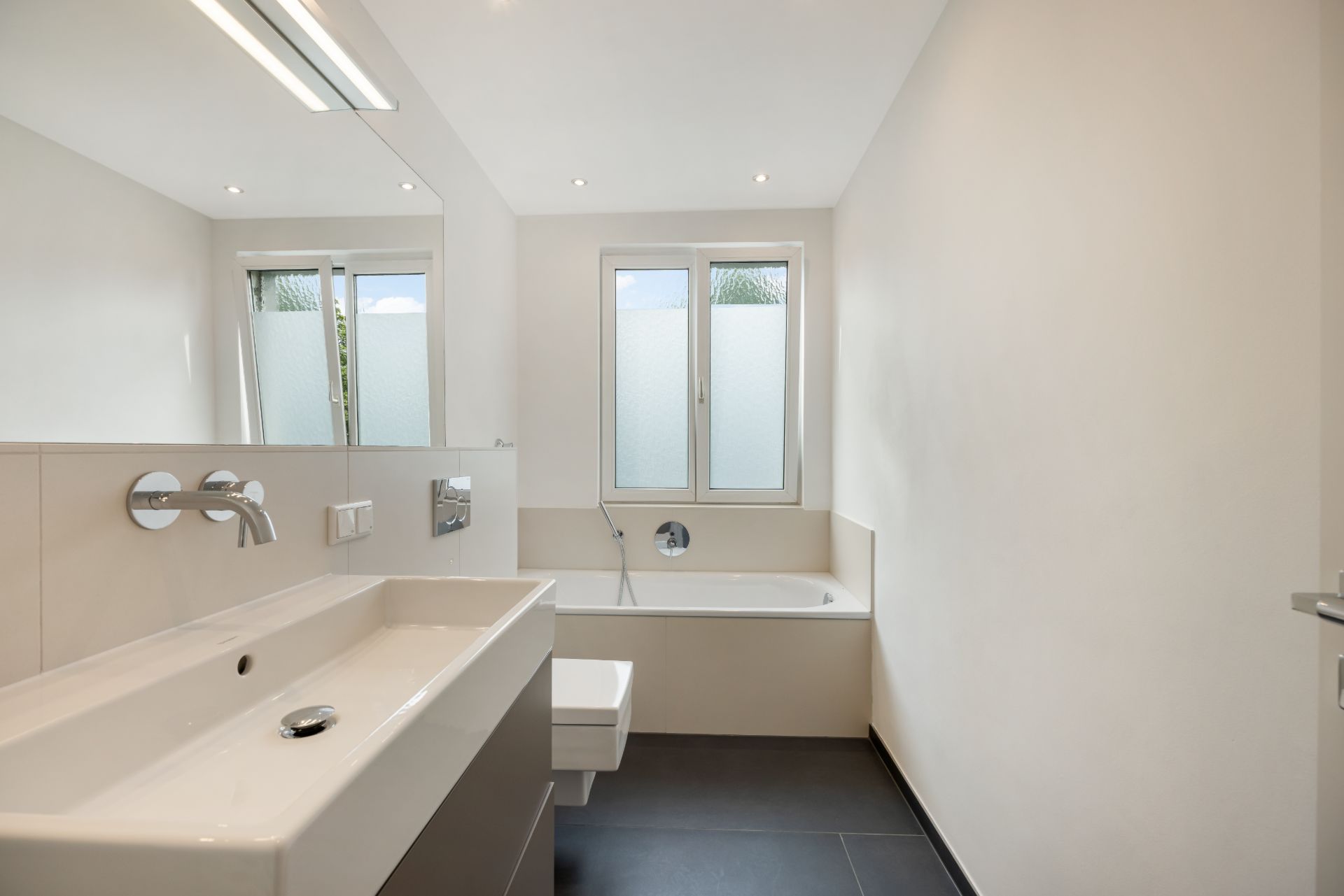 Modernes Badezimmer mit Waschbecken, Badewanne und großem Fenster.