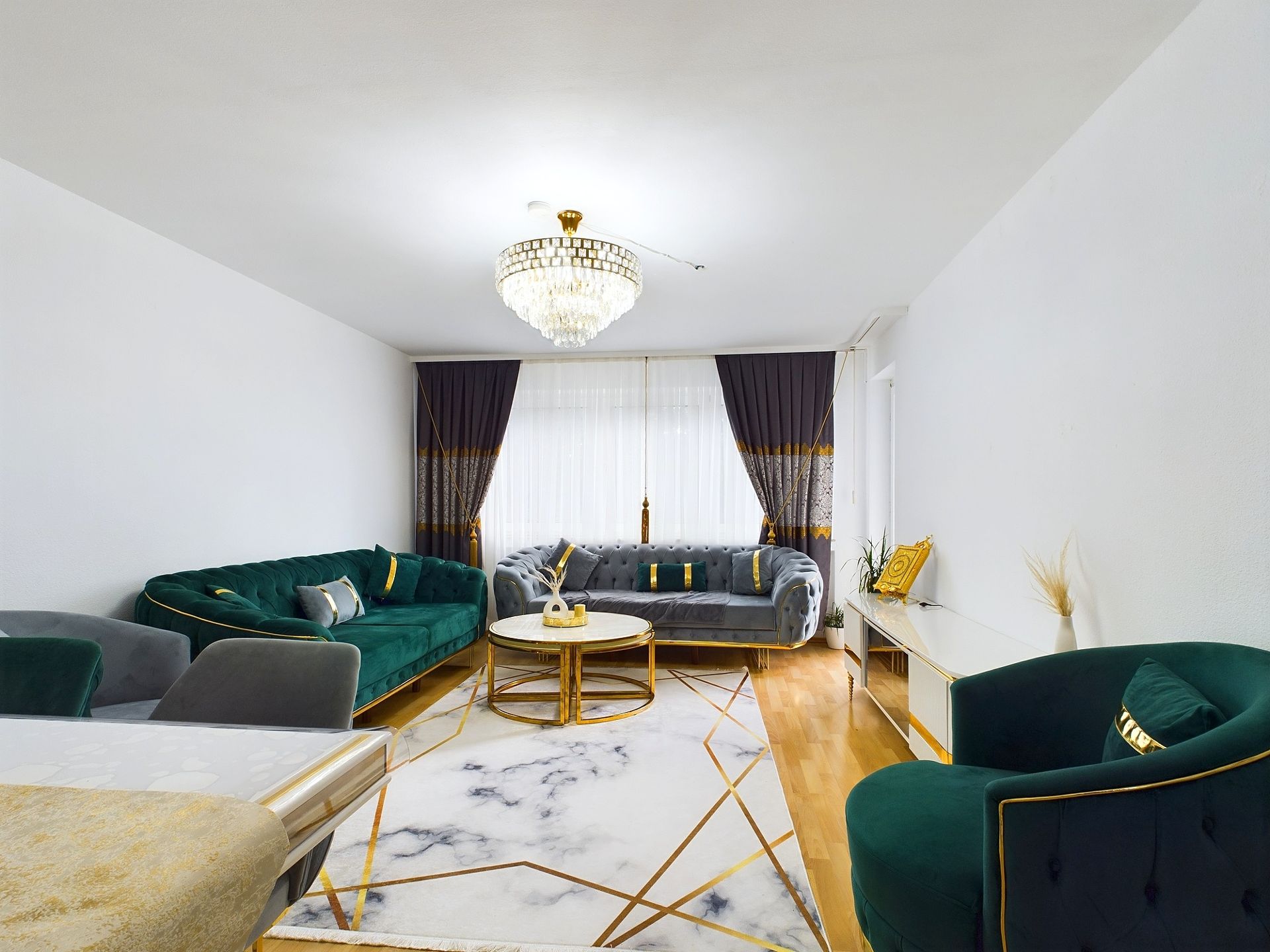 Modernes Wohnzimmer mit grünen Sofas, Marmorteppich und Kronleuchter.