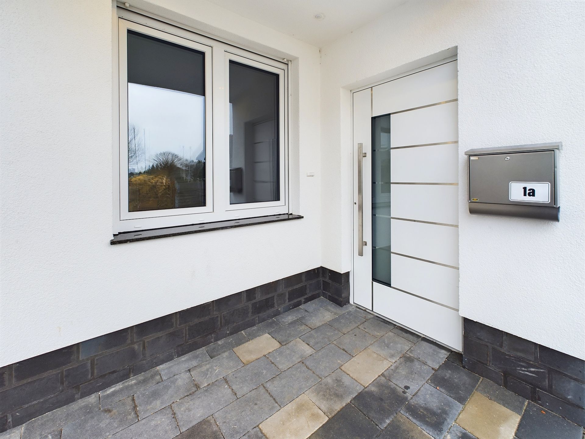 Hauseingang mit moderner weißer Tür, Fenster und Briefkasten an weißer Wand.