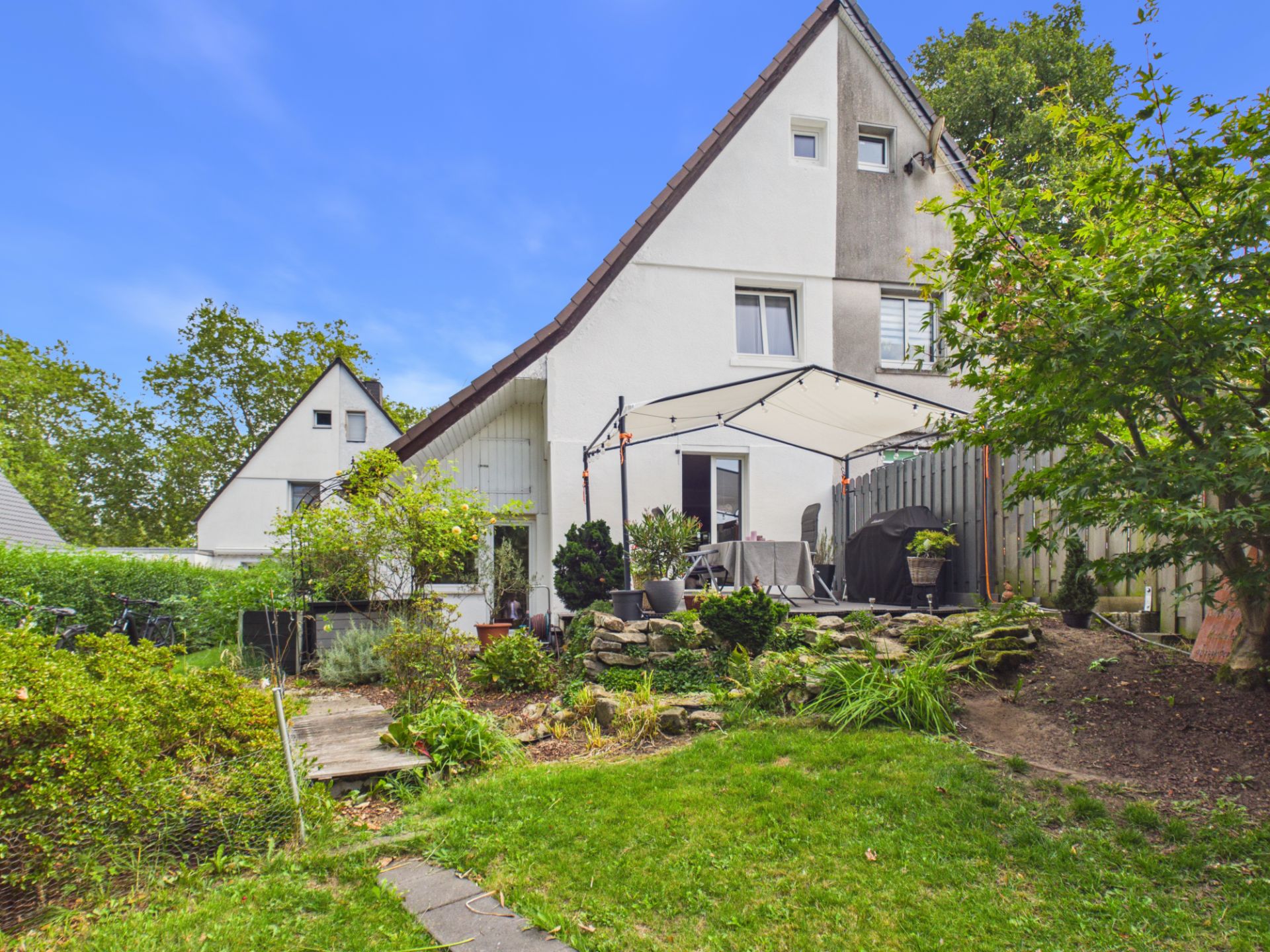 Garten mit Sitzbereich, Pflanzen und weißem Wohnhaus im Hintergrund.