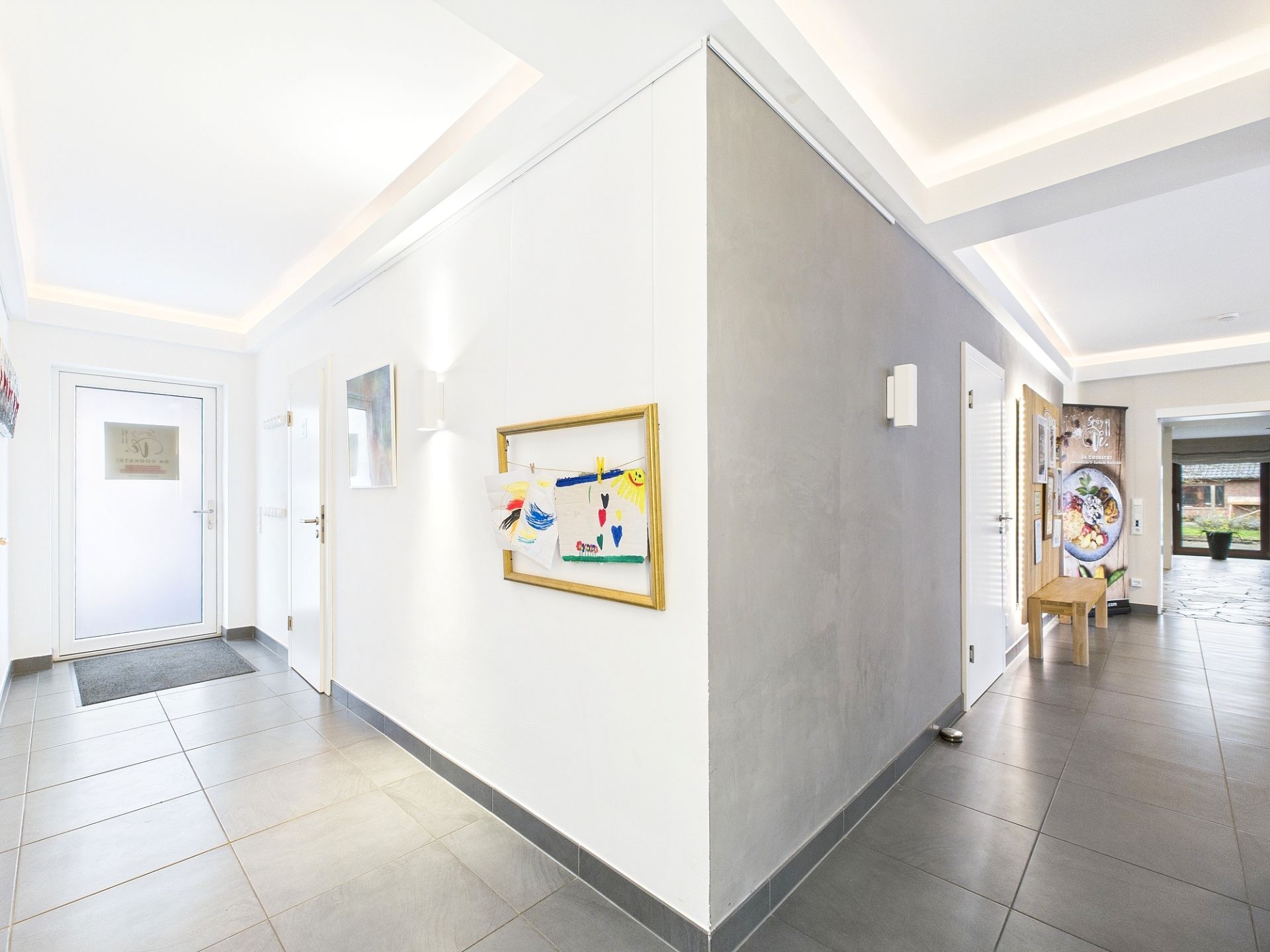 Heller Flur mit grauen Fliesen, weißen Wänden und Kinderzeichnungen an der Wand.