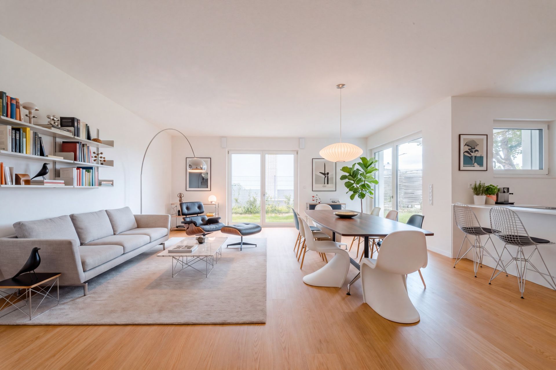 Helles Wohnzimmer mit Sofa, Esstisch, Stühlen und großen Fenstern, moderne Einrichtung.