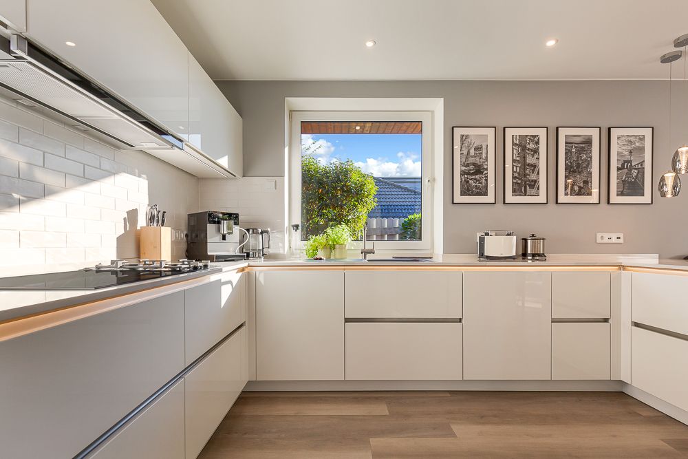 Helle, moderne Küche mit weißen Schränken, Holzboden und Fenster mit Blick nach draußen.