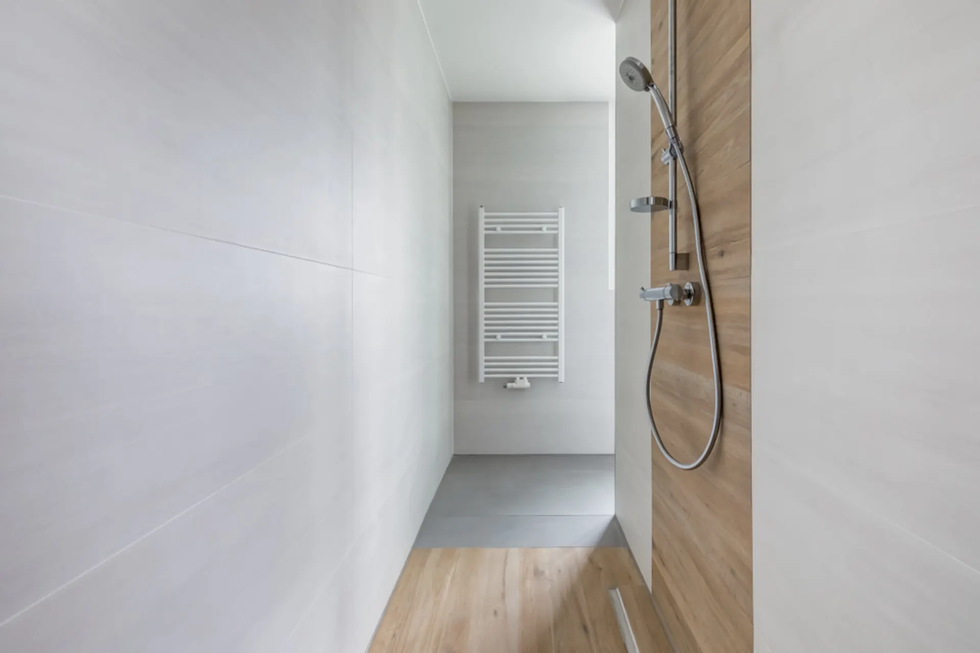 Moderne, minimalistische Dusche mit Holz- und weißen Fliesen, Duschkopf und Heizkörper.