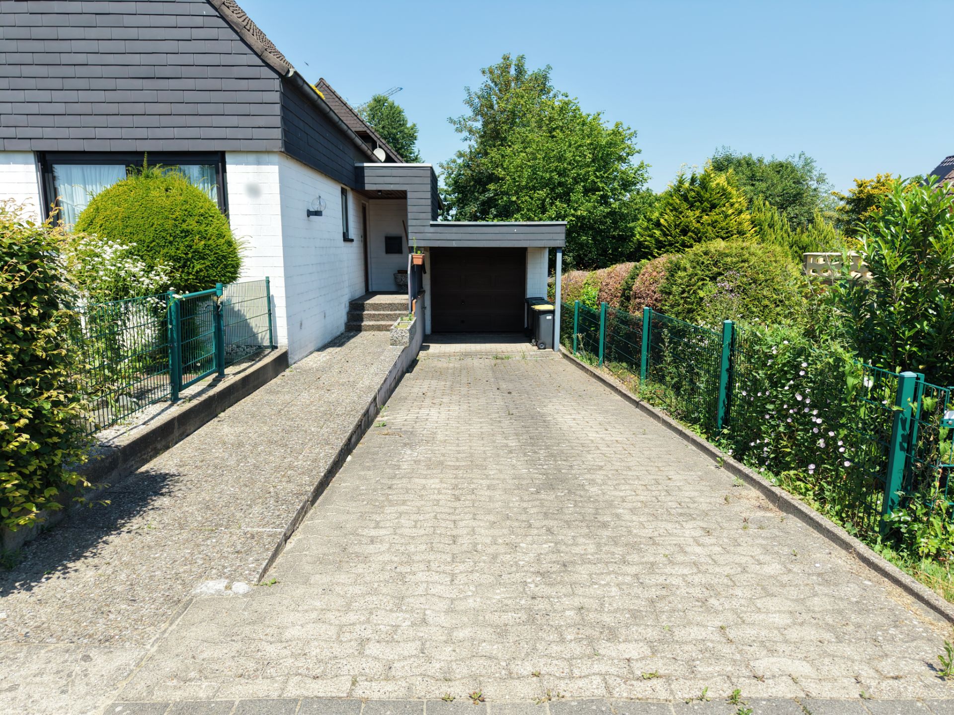 Gepflasterte Einfahrt mit angrenzender Garage und bepflanztem Garten an einem Wohnhaus.