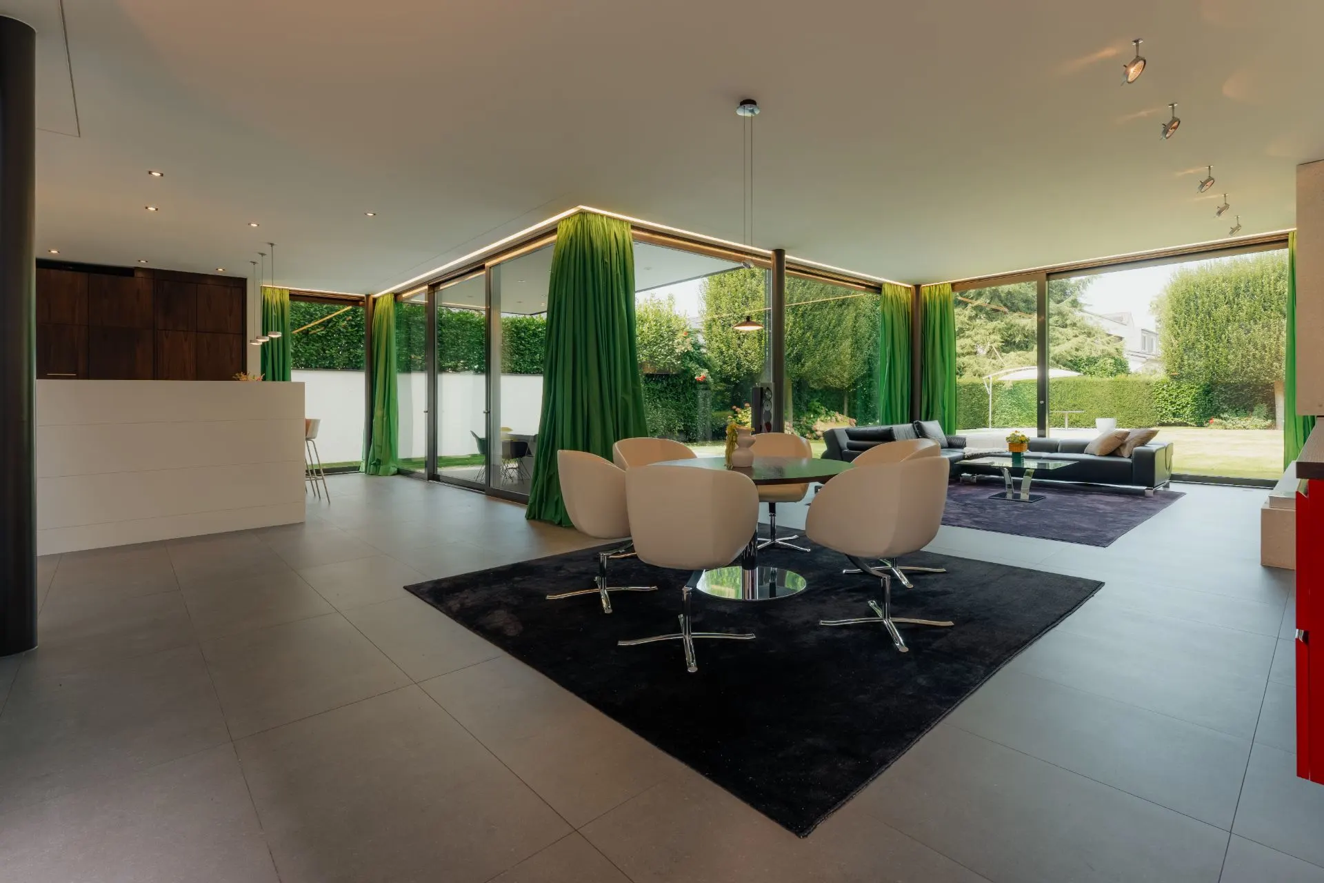 Modernes Wohnzimmer mit großen Fenstern, grünen Vorhängen und weißen Sesseln auf dunklem Teppich.