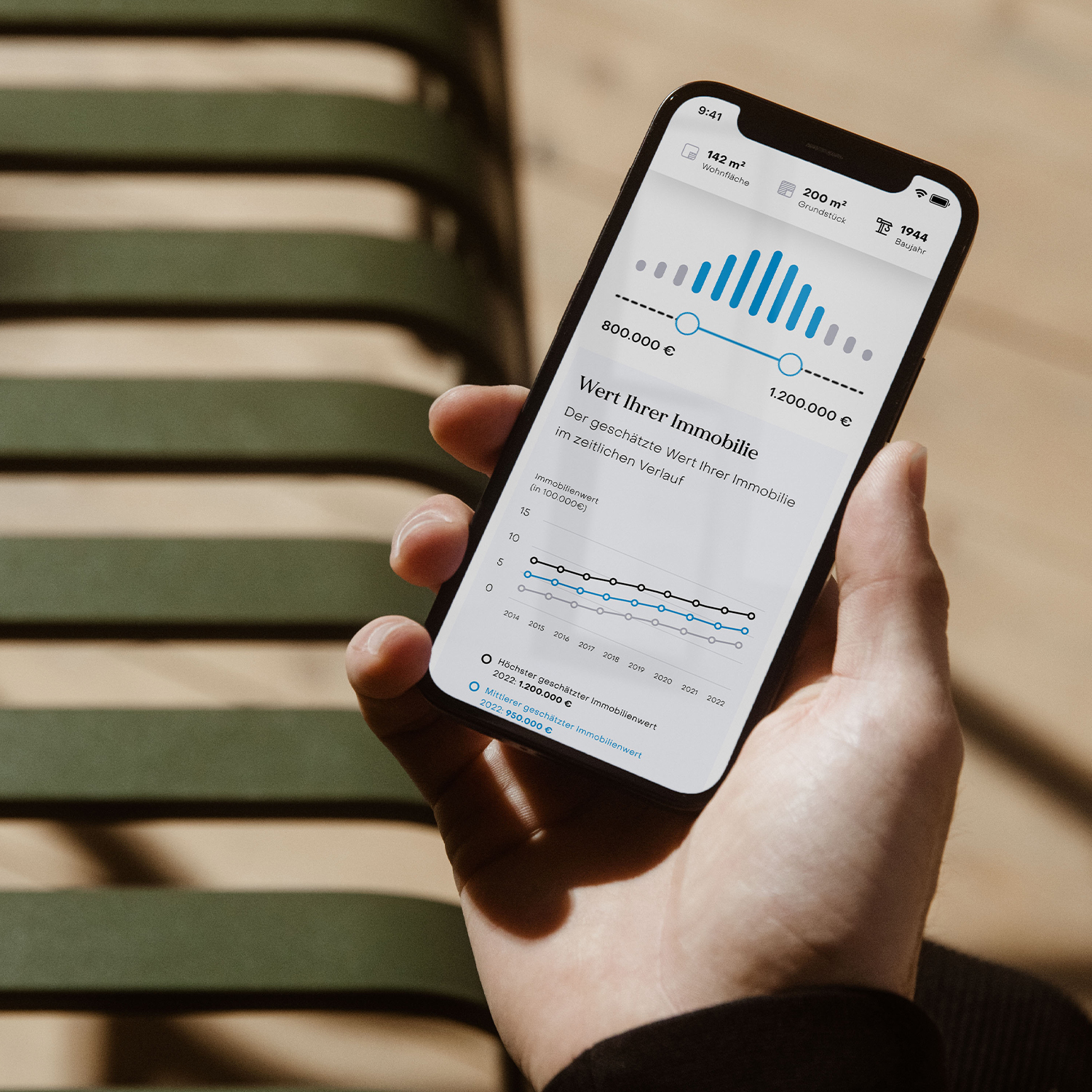 Person hält Smartphone mit Diagrammen und Zahlen zur Immobilienbewertung in der Hand.