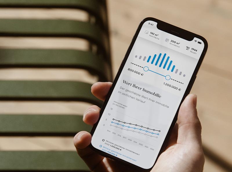 Person hält Smartphone mit Diagrammen und Zahlen zur Immobilienbewertung in der Hand.