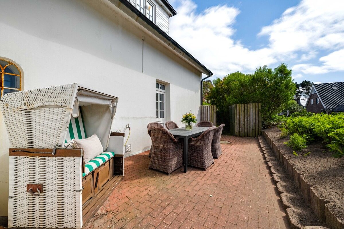 Terrasse mit Sitzgruppe und Strandkorb an einem Wohnhaus, umgeben von Pflanzen.