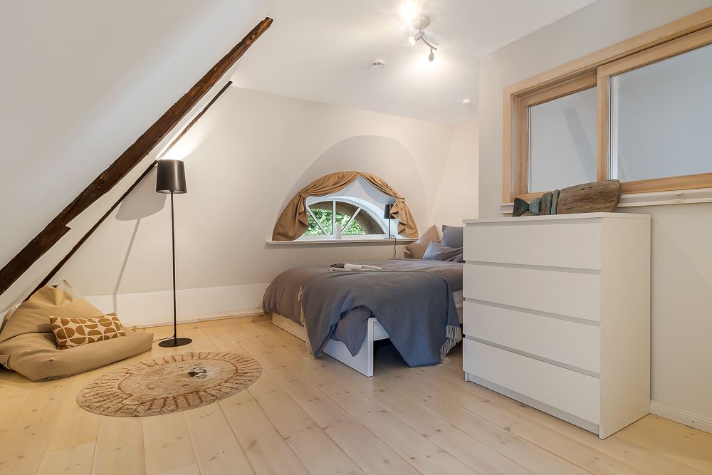 Helles Schlafzimmer mit Bett, Kommode, Sitzsack und rundem Teppich im Dachgeschoss.