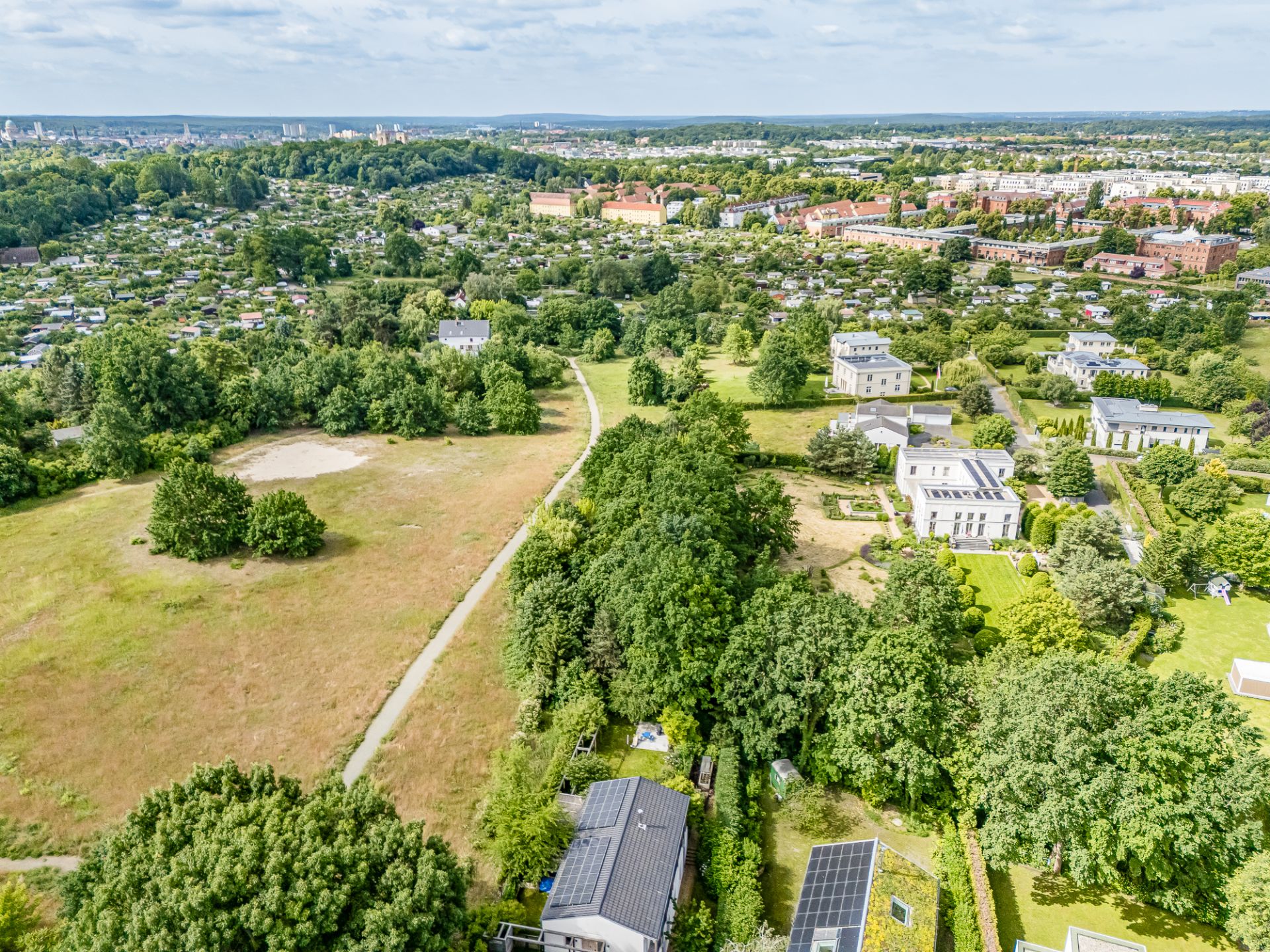 Luftaufnahme von Wohnhäusern mit viel Grün und angrenzender Wiese.