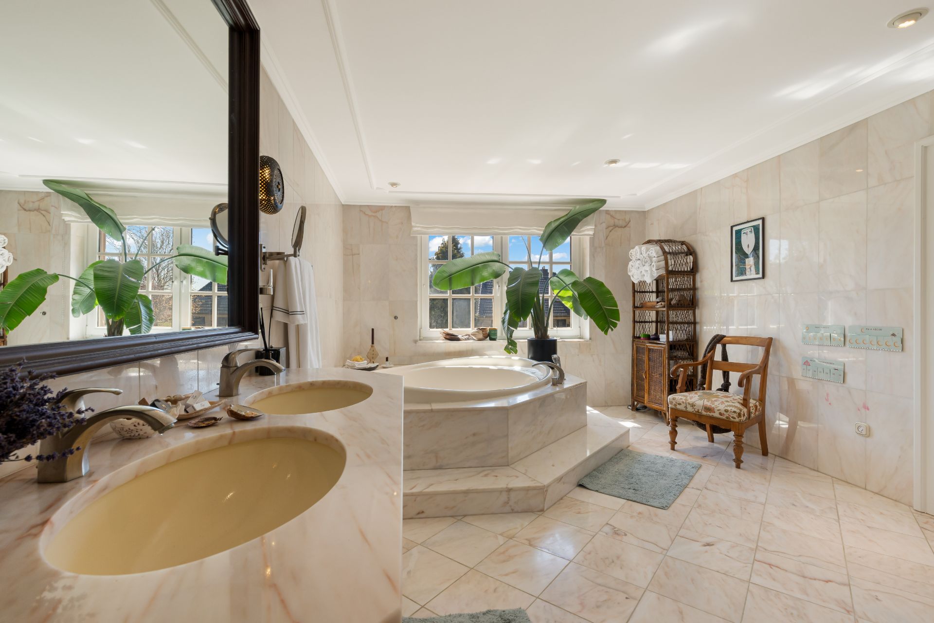 Helles Badezimmer mit großer Badewanne, Doppelwaschbecken, Pflanzen und einem Fenster.