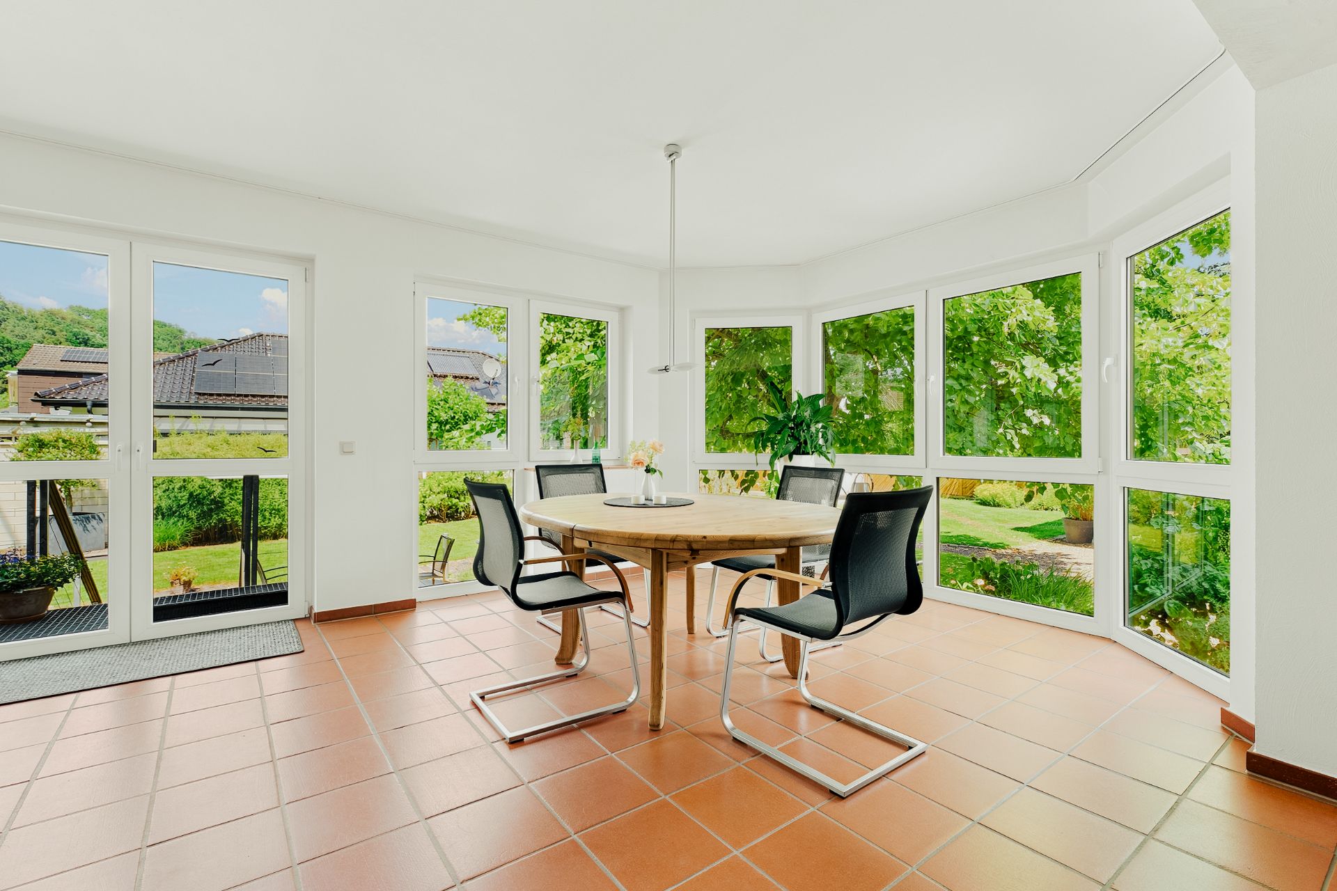 Heller Essbereich mit rundem Holztisch, vier Stühlen und großen Fenstern mit Gartenblick.