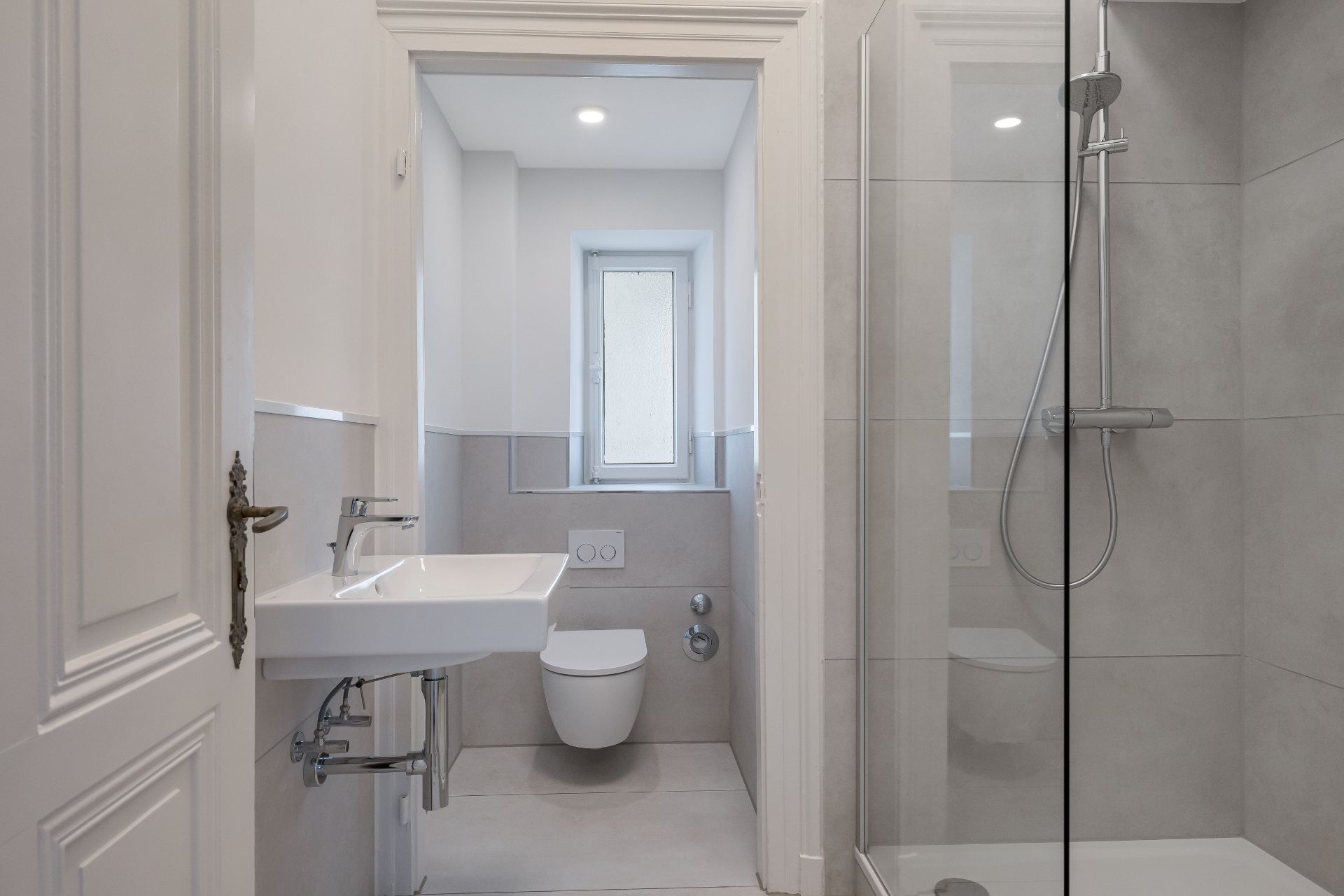 Modernes Badezimmer mit Waschbecken, Wandtoilette, Fenster und verglaster Dusche.
