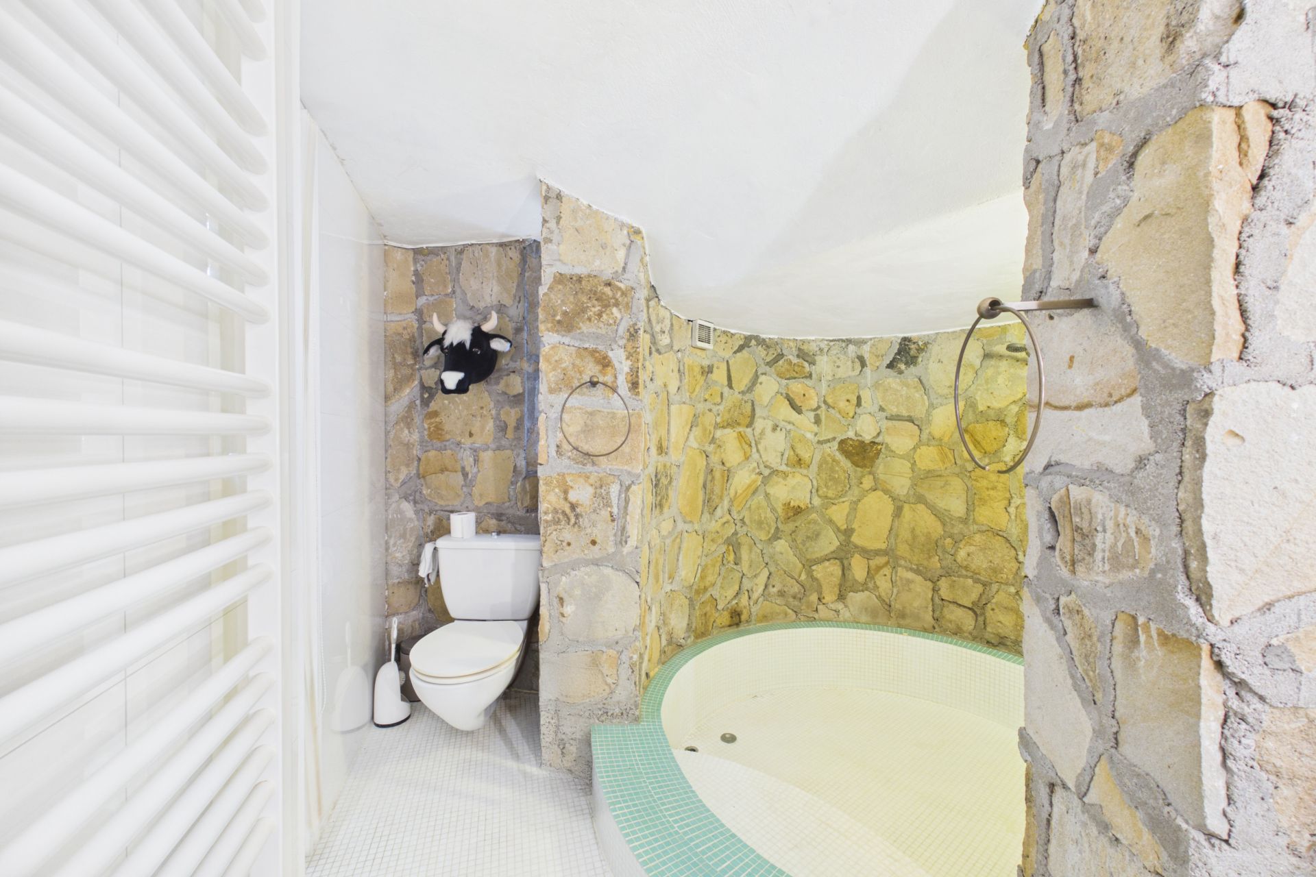 Badezimmer mit Steinen, runder Badewanne, Toilette und Handtuchhalter.