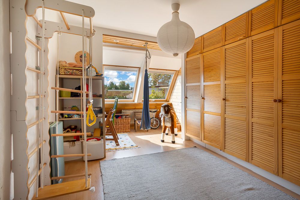 Helles Kinderzimmer mit Spielzeug, Kletterwand, Schränken und großen Fenstern.