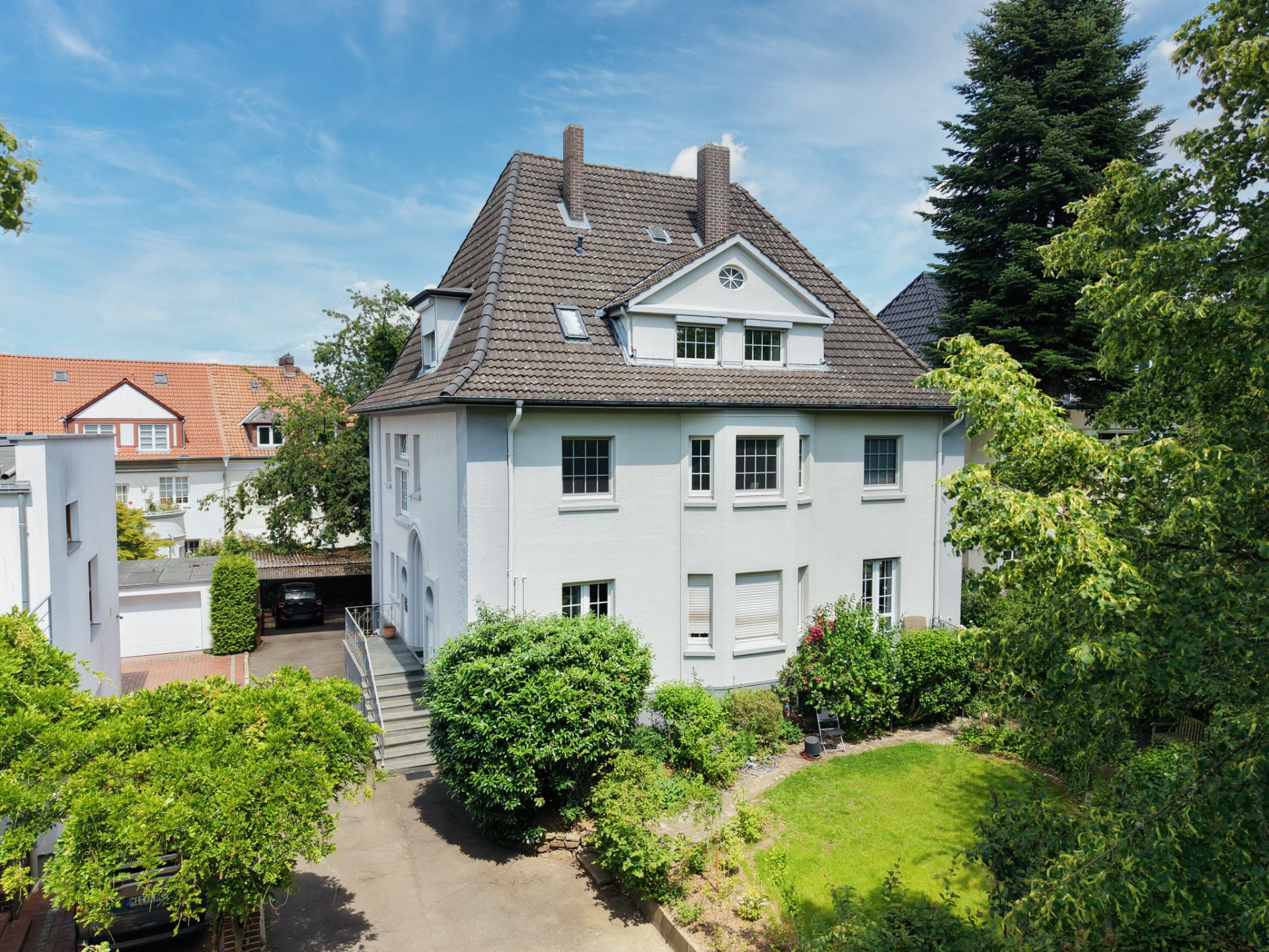 Weißes Wohnhaus mit Satteldach, vielen Fenstern und grünem Vorgarten.