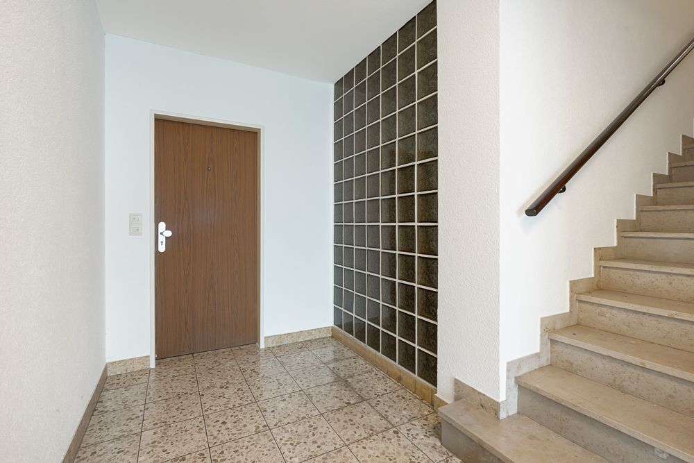 Hausflur mit brauner Eingangstür, Treppe und Wand aus Glasbausteinen.