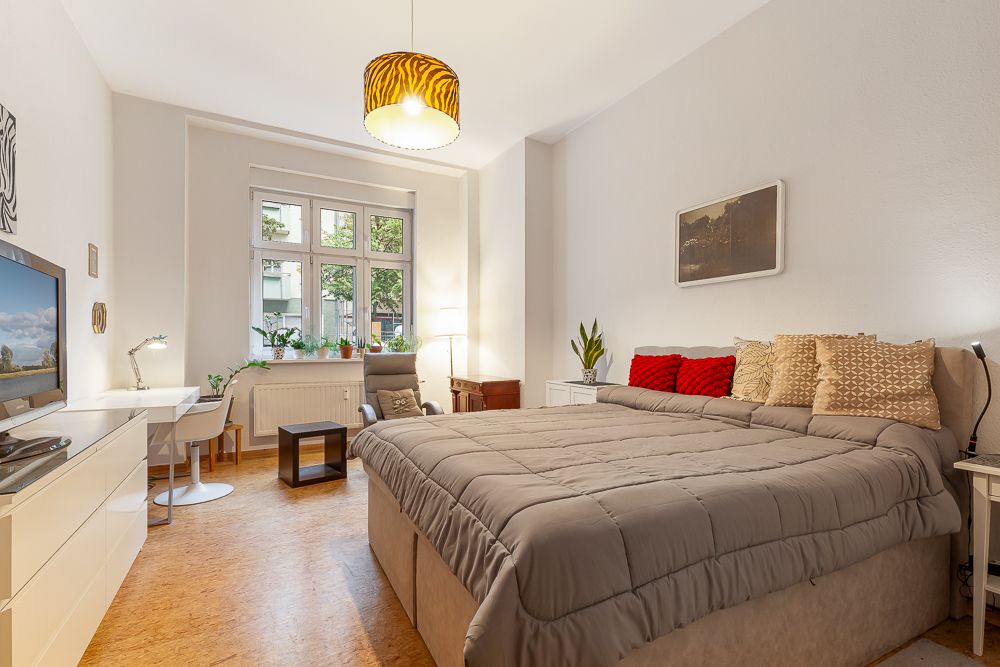 Helles Schlafzimmer mit großem Bett, Sessel, Schreibtisch und Fenster mit Blick ins Grüne.