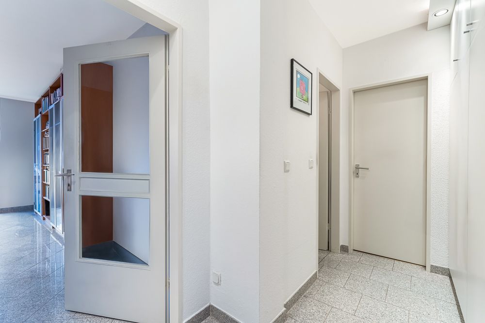 Heller Flur mit Fliesenboden, drei weißen Türen und einem Bild an der Wand.