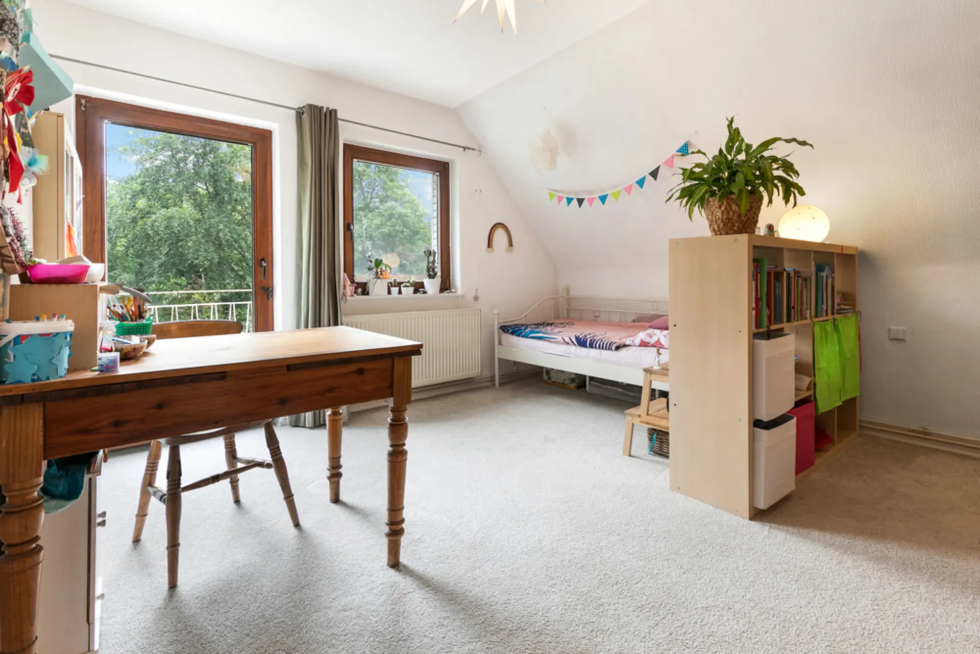 Helles Kinderzimmer mit Schreibtisch, Regal, Bett und zwei Fenstern mit Blick ins Grüne.