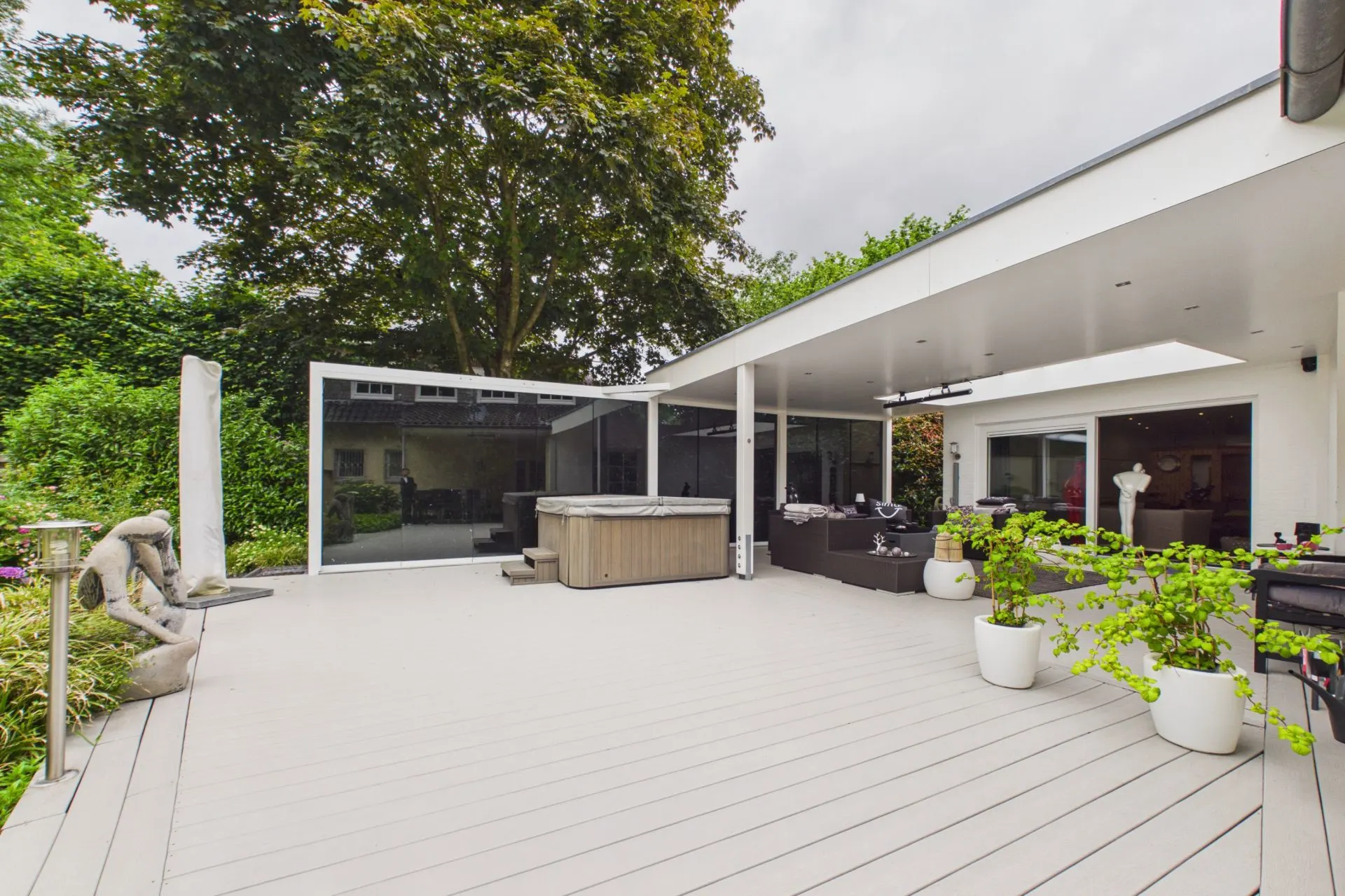 Große moderne Terrasse mit Whirlpool, Sitzbereich und Pflanzen in weißen Töpfen.