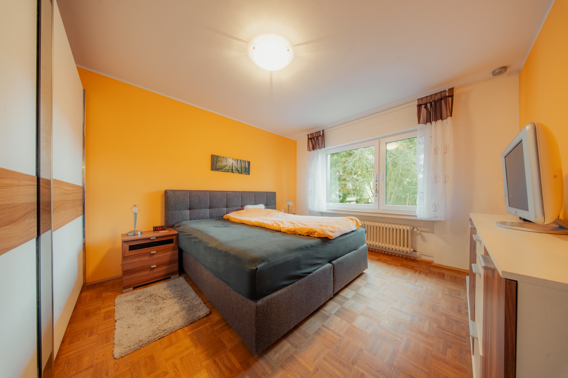 Schlafzimmer mit Doppelbett, Nachttischen, Fernseher und großem Fenster mit Blick ins Grüne.