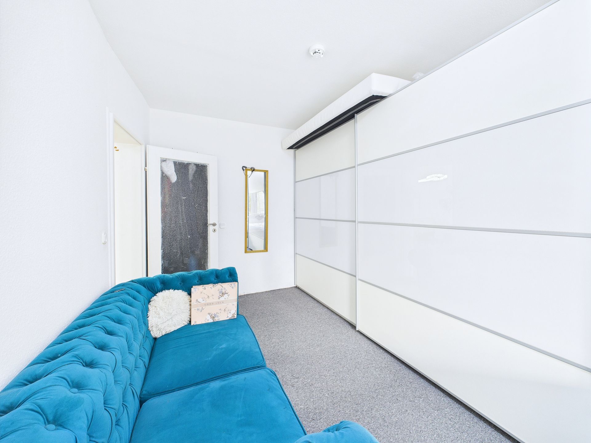 Helles Zimmer mit blauem Sofa, großem weißen Schrank und Wandspiegel.
