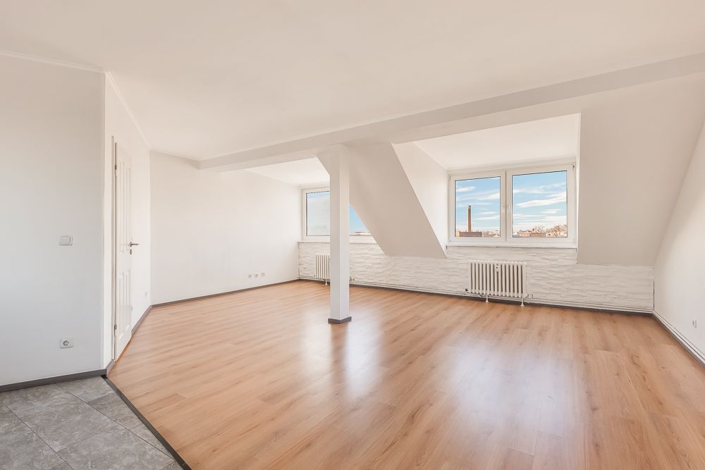 Helles leerstehendes Zimmer mit Holzfußboden, weißen Wänden und zwei Fenstern.