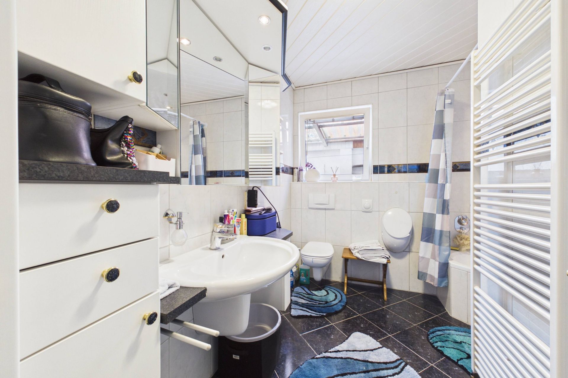 Modernes Badezimmer mit Waschbecken, Spiegel, Toilette, Badewanne und gemusterten Teppichen.