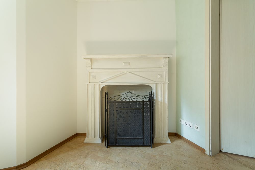 Weißer Kamin mit schwarzem Funkenschutzgitter in einer Ecke eines Raumes.